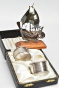 A BOXED SET OF TWO SILVER NAPKIN RINGS AND A WHITE METAL MODEL OF A BOAT, the napkin rings each with