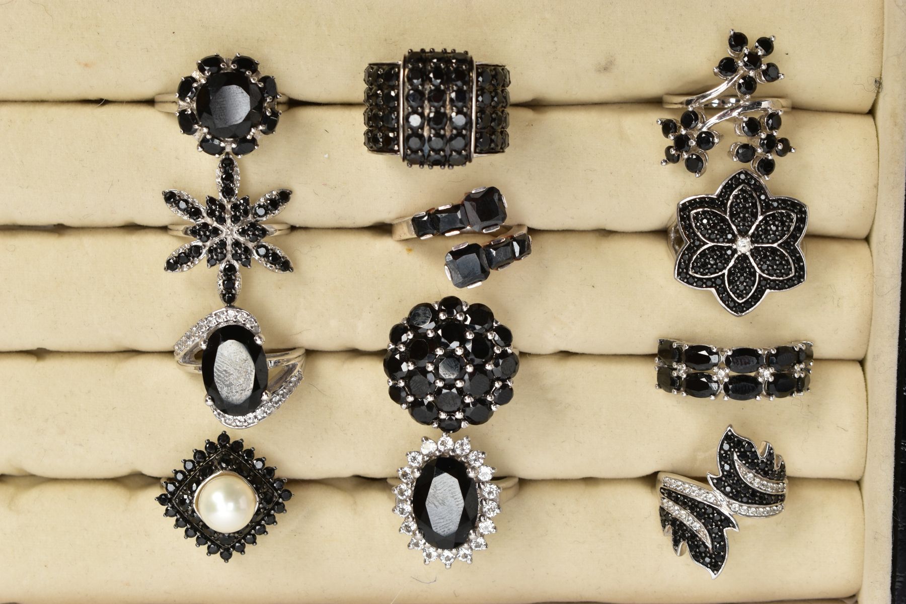 TWELVE BLACK SPINEL RINGS AND A RING BOX, of various designs such as clusters, crossover, half