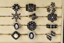 TWELVE BLACK SPINEL RINGS AND A RING BOX, of various designs such as clusters, crossover, half