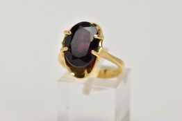 A YELLOW METAL GARNET DRESS RING, designed with a four claw set, oval cut garnet, within a concave