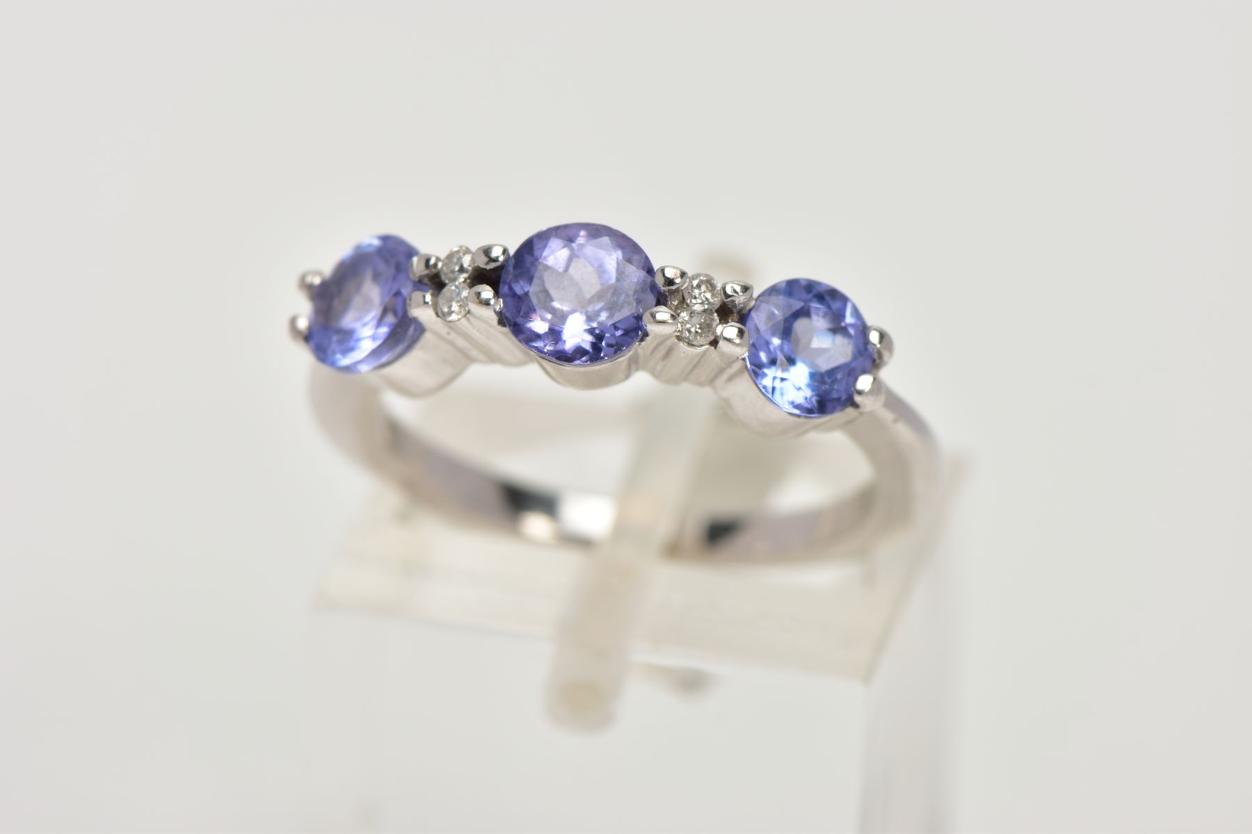 A TANZANITE AND DIAMOND RING, designed as three circular cut tanzanites each interspaced by two