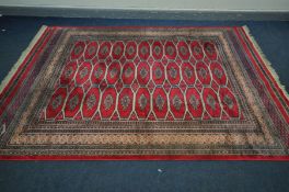 A 20TH CENTURY WOOLLEN GROUND RUG, of a geometric design, red field and multistrap border, 305cm x