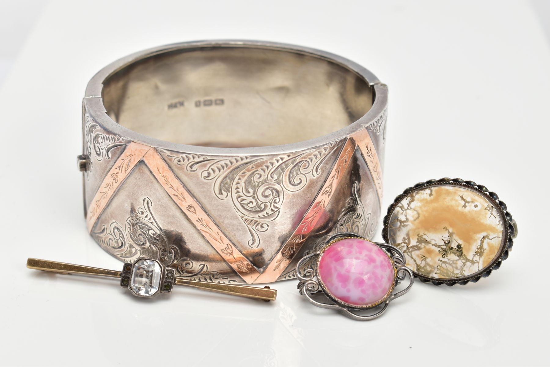 A SILVER HINGED BANGLE AND THREE BROOCHES, the wide hinged bangle, decorated with a foliate design