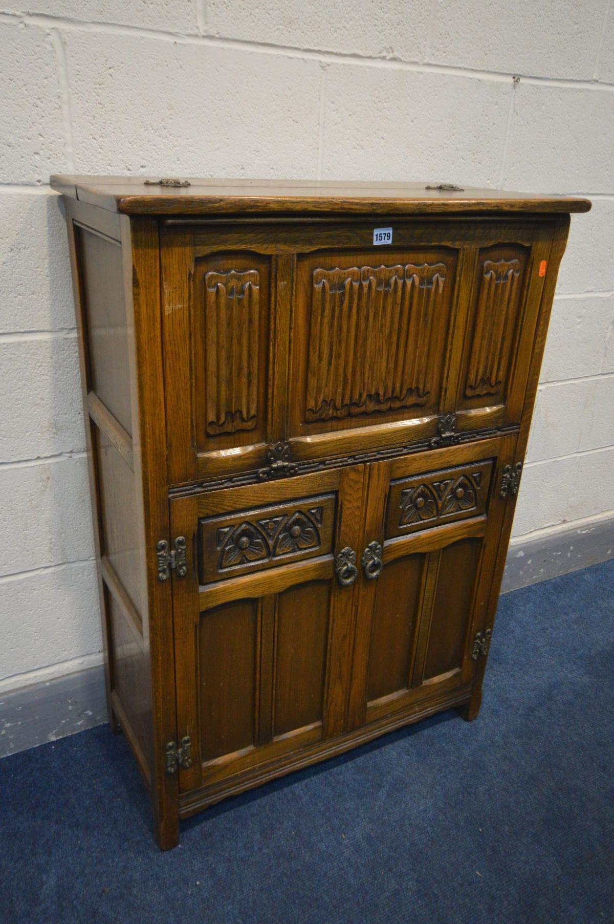 AN OLD CHARM OAK LINENFOLD COCKTAIL CABINET, the hinged top and fall front with a mirror back and