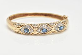 A 9CT GOLD SAPPHIRE AND DIAMOND HINGED BANGLE, set with three oval cut blue sapphires each within