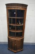 A REPRODUCTION MAHOGANY BOWFRONT GLAZED SINGLE DOOR CORNER CUPBOARD, over double cupboard doors,