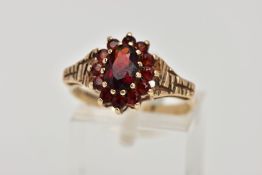 A 9CT GOLD GARNET DRESS RING, slightly raised cluster of an oval design, set with a central oval cut