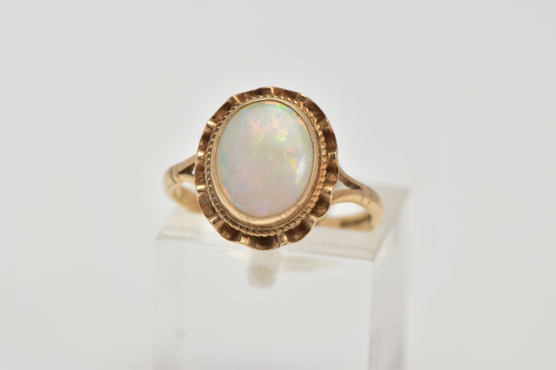 A 9CT GOLD OPAL DRESS RING, designed as an oval cabochon within a collet mount, swag surround,