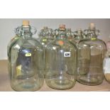 ELEVEN GLASS DEMI JOHNS, ten in clear glass, seven of which have cork bungs, one demi john in