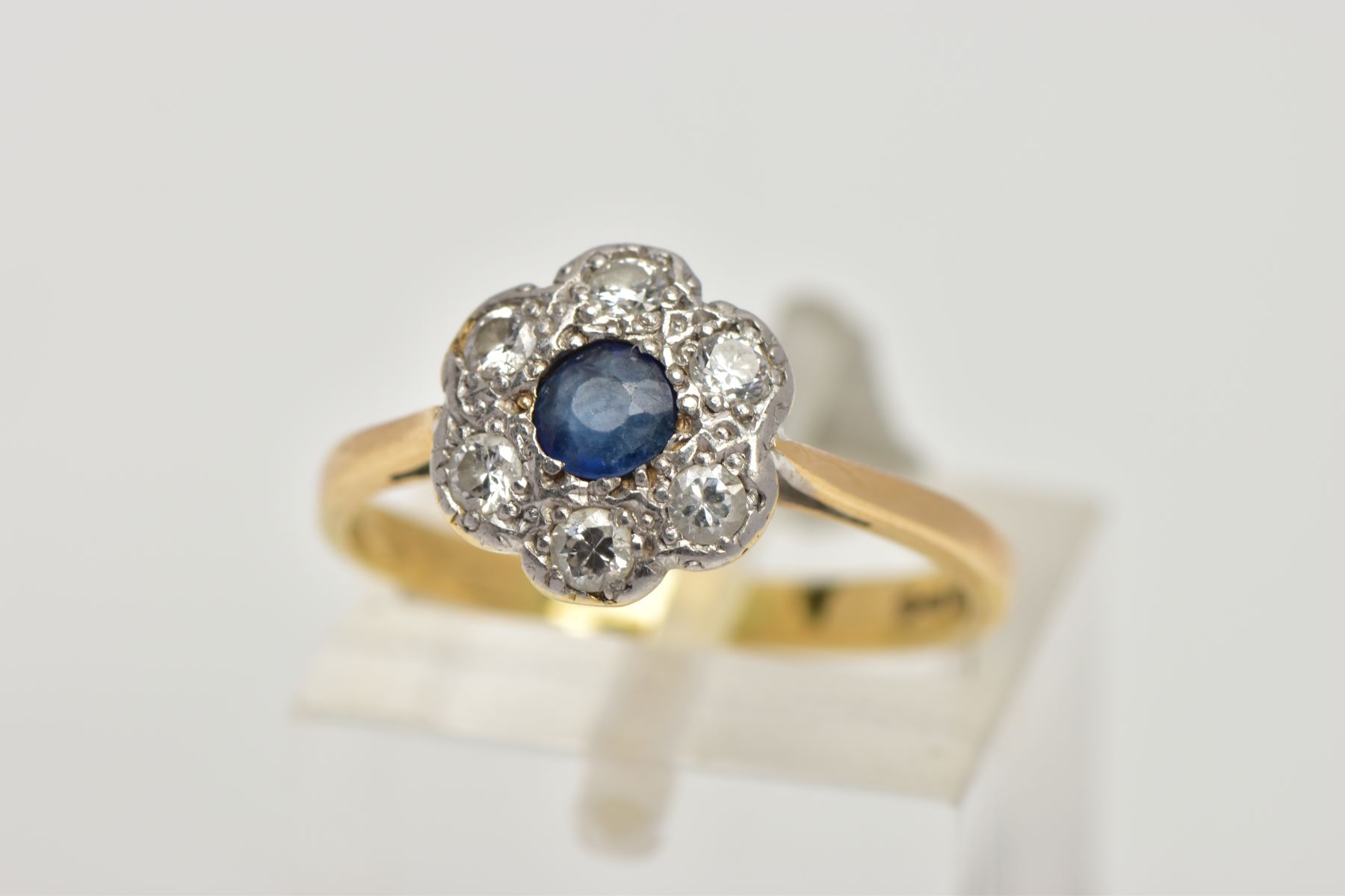 AN 18CT GOLD SAPPHIRE AND DIAMOND CLUSTER RING, of a flower shape, centring on a circular cut blue