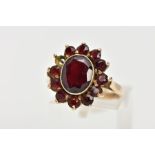 A 9CT GOLD GARNET CLUSTER RING, of an oval form, centring on a collect mounted oval cut garnet,