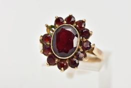 A 9CT GOLD GARNET CLUSTER RING, of an oval form, centring on a collect mounted oval cut garnet,