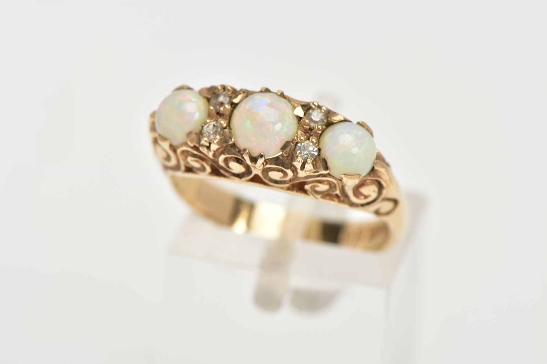 A THREE STONE OPAL RING, three circular opals set in a raised mount with scrolling detail,