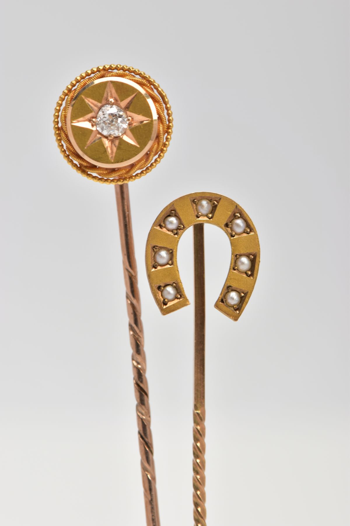TWO GOLD STICK PINS, one stick pin featuring a horse shoe design set with seven seed pearls,