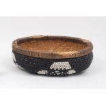 A Zambian beaded basket, 20th century, of circular form, the woven body with beaded cover, with