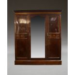An Edwardian mahogany and inlaid triple wardrobe, the moulded cornice above central mirrored door