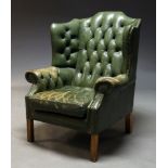 A George III style wing back arm chair, with button back green leather upholstery and brass stud