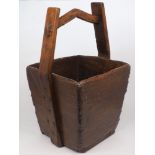 A Chinese hardwood rice bucket, of quadrilateral form with arching handle and metal bosses, 60cm