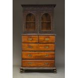 A Lamu cabinet on two section chest base, the foliate carved cabinet top with two glazed doors