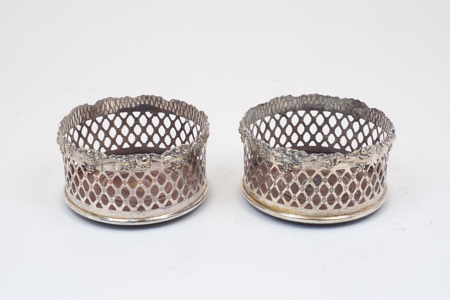 A pair of silver plated wine bottle coasters with turned wooden bases, the pierced sides to rim