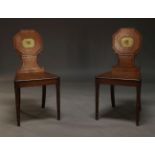 A pair of Regency mahogany hall chairs, with octagonal backrests centred by painted cartouche