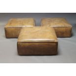A set of three large leather upholstered poufs, of recent manufacture, of square form, upholstered