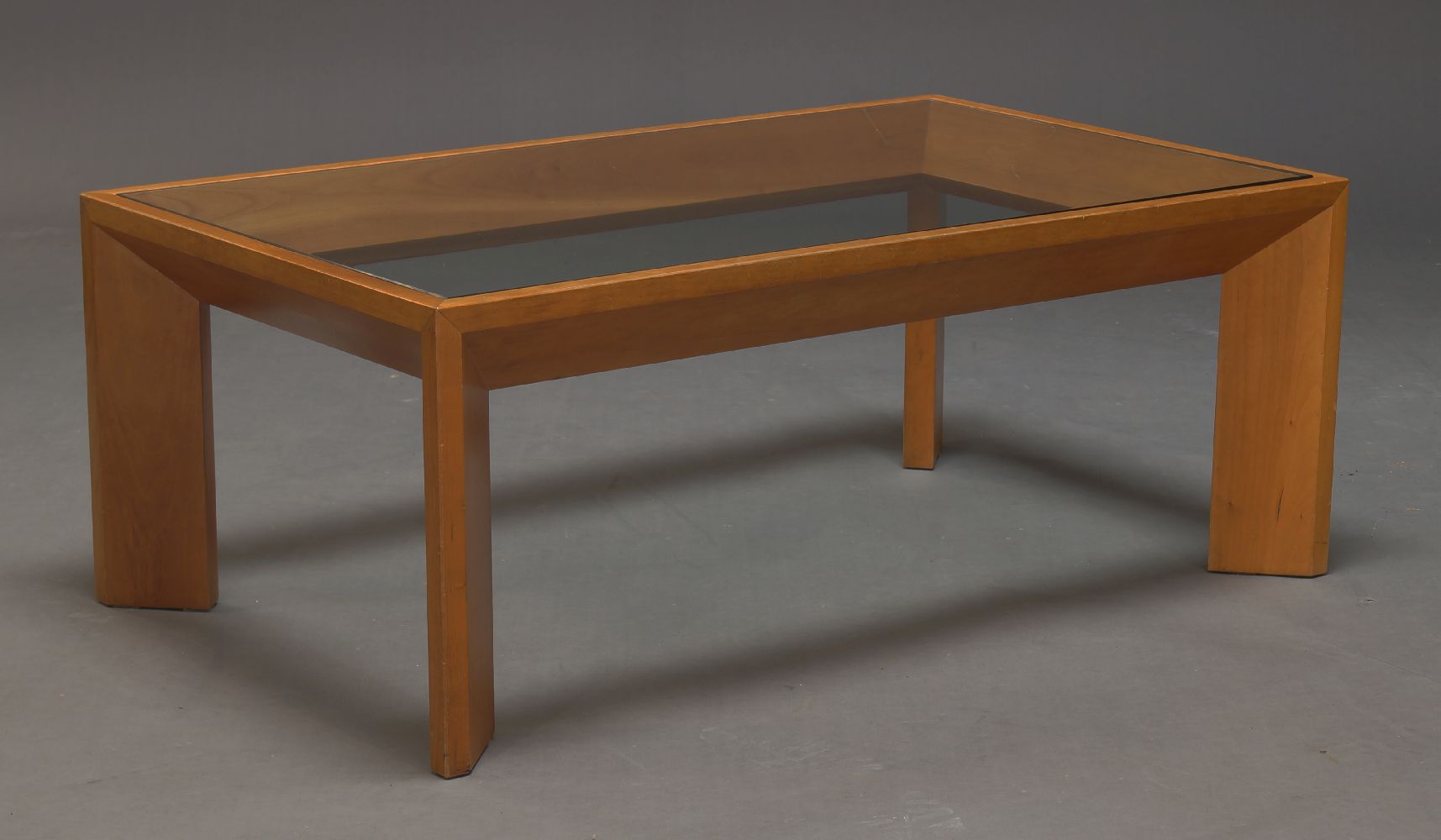 A modern cherry wood and glazed coffee table, the rectangular glazed top on chamfered angled