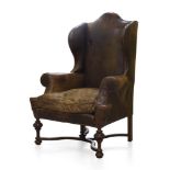 A brown leather wingback armchair, mid 20th century, with serpentine wings and scrolling arms