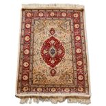 A Hereke silk rug, mid to late 20th century, with red pole medallion in an ivory floral and