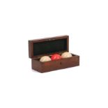 Three billiard balls, Edwardian, each ball carved in ivory, one stained red, in suited mahogany case