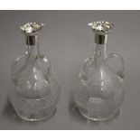 A pair of Edwardian glass and silver table carafes with three handles to the body,
