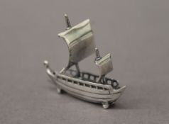 A small silver model of a ship. 3.5 cm long.