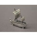 A small silver model of a ship. 3.5 cm long.