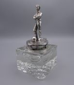 A silver plate mounted glass inkwell, the lid surmounted with a footballer. 17 cm high.