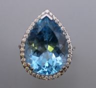 An 18 ct white gold ring set with a pear shaped aquamarine surrounded by small diamonds.