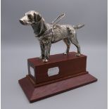 A silvered bronze model of a guide dog, possibly a car mascot, on display plinth.