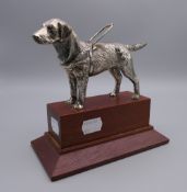 A silvered bronze model of a guide dog, possibly a car mascot, on display plinth.