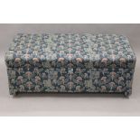 An upholstered ottoman. 106 cm wide.