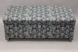 An upholstered ottoman. 106 cm wide.