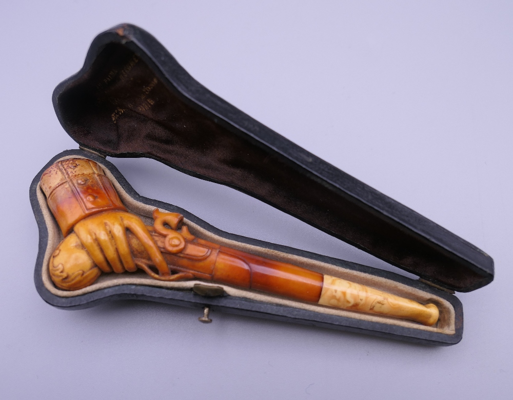 A cased 19th century meerschaum and amber pipe formed as a hand holding a pistol. 12 cm long.