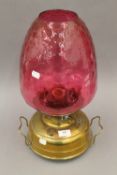A Victorian brass oil lamp with cranberry shade. 45 cm high.