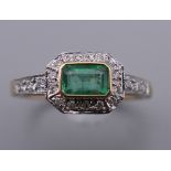An Art Deco style 9 ct gold emerald and diamond ring, with diamond set shoulders and engraved shank.