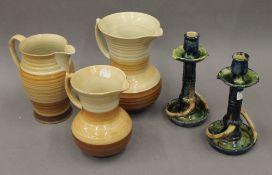 Three Shelley jugs, the largest 23 cm high, and a pair of slipware Arts & Crafts candlesticks.