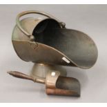 A copper coal scuttle, a coal shovel, a brass oil lamp and a warming pan.