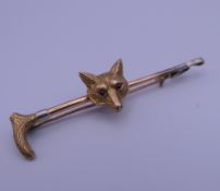 A 9 ct gold ruby set fox mask and riding crop bar brooch, housed in an Asprey box. 5.5 cm wide. 4.