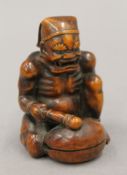 A boxwood okimono formed as a figure banging a drum. 7.5 cm high.