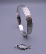 A silver bangle decorated with nursery rhyme animals and a silver enamel fish form charm.