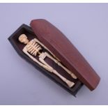 A bone model of a skeleton in a wooden coffin. 11.5 cm long.
