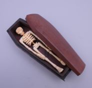 A bone model of a skeleton in a wooden coffin. 11.5 cm long.