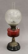 A Victorian oil lamp with cranberry glass reservoir. 56 cm high overall.